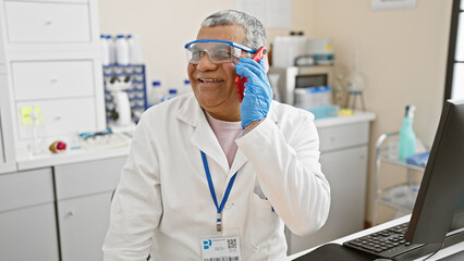 Smiling middle-aged man in lab coat talking on phone in laboratory