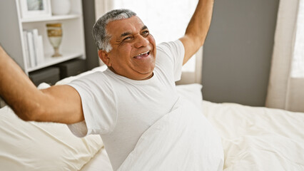 A cheerful mature man waking up and stretching in his bedroom, signifying a fresh start to his day.