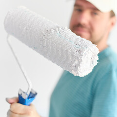Young man holding a roller in front of himd - small depth of field.  The idea of painting the walls white.