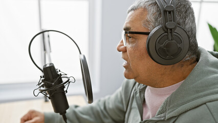 Senior man with headphones speaking into a microphone in a radio studio setting