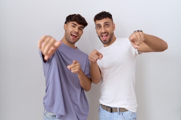 Homosexual gay couple standing over white background pointing to you and the camera with fingers, smiling positive and cheerful