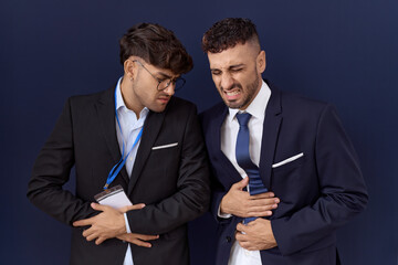Two hispanic business men wearing business clothes with hand on stomach because nausea, painful...