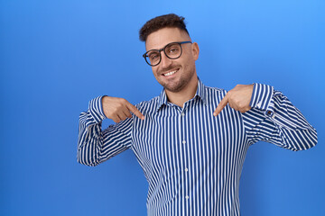 Hispanic man with beard wearing glasses looking confident with smile on face, pointing oneself with...