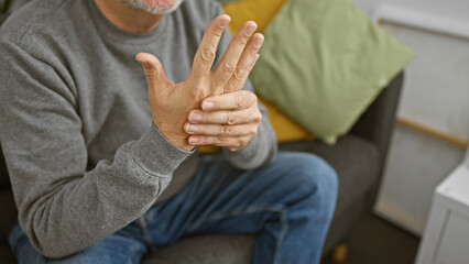 A grey-haired man experiencing wrist pain in a cozy home setting.