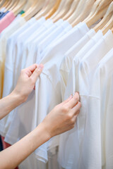 Close up of woman hand choosing discount t-shirt clothes in store at shopping mall