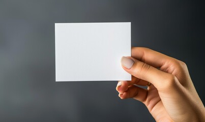 Obraz premium Hand holding blank white card on gray background - A close-up photo of a hand holding a blank white card against a neutral gray background, explicitly emphasizing clarity and potential