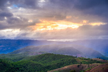 amazing dramatic raining clouds in sunset with sun rays over misty mountains landscape  