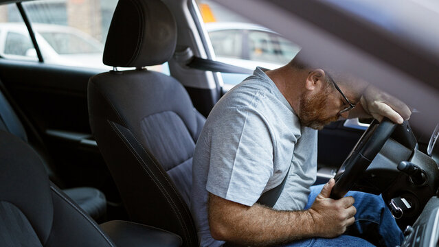 Handsome middle-aged caucasian man, with a beard, exudes stress while driving a car on a busy urban street, depicting an unhappy and anxiety-filled journey.