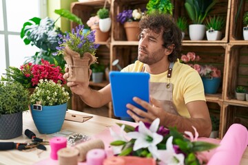 Young hispanic man florist using touchpad holding lavender plant at flower shop