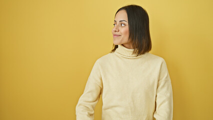 Portrait of a smiling young hispanic woman in a cream sweater, isolated against a yellow...