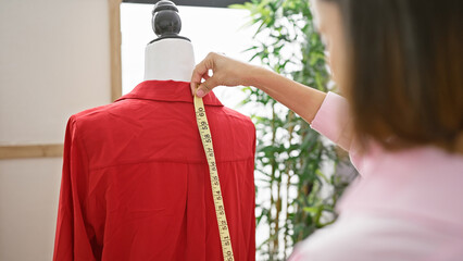 Woman tailor measuring red garment on mannequin in bright workshop