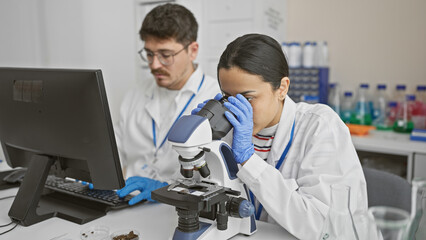 Man and woman scientists collaborate in a laboratory, with a microscope and samples while using...