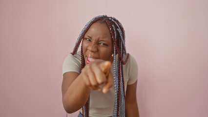 An expressive african woman with braided hair pointing towards the camera against a pink background.