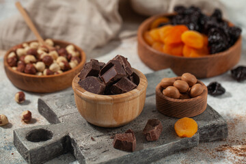 Cubes of dark artisan chocolate. Assorted nuts, dark chocolate, and dried fruits on stone
