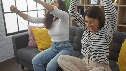 Two joyful women celebrating in a cozy living room, expressing happiness and a close relationship...