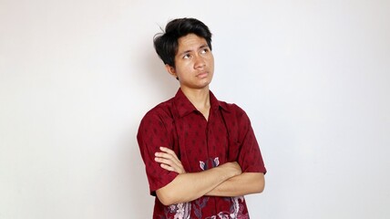 Handsome young Asian man in batik is posing with crossed arms and looking up as if he is thinking about something