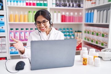 Young arab woman working at pharmacy drugstore using laptop looking at the camera smiling with open...
