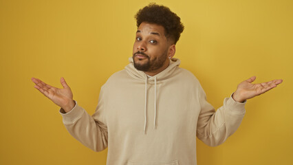 Confused african american man in hoodie against yellow background shrugging