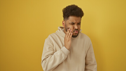 African american man with toothache isolated on yellow background, expressing pain and discomfort...