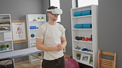 A young hispanic man wearing vr goggles stands contemplatively in a modern rehabilitation clinic's room.