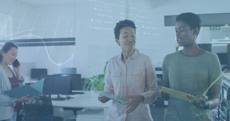Image of stock market data processing over two diverse women discussing while walking at office