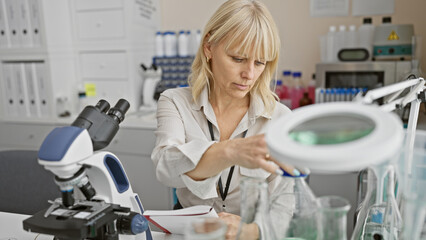 Blonde woman scientist using microscope in laboratory setting, portraying focus and professionalism.