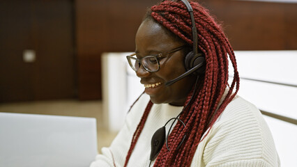 Smiling african american woman with braids wearing headset working in an office indoor setting.