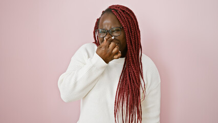 A woman with braids expresses disgust over a pink background, covering her nose with her hand. - obrazy, fototapety, plakaty