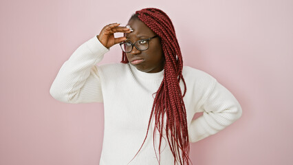 Thoughtful african american woman with braids wearing glasses and white sweater against a pink...