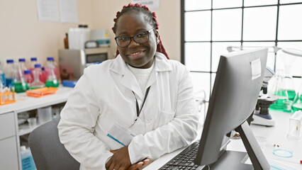 African american woman with braids working in a laboratory, smiling confidently at the camera.