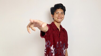 Excited handsome Asian young man wearing a batik shirt and smiling kindly pointing to the front of...