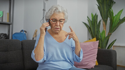 Elderly woman using phone in a modern living room, expressing confusion