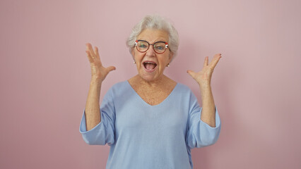 Excited senior woman with grey hair wearing glasses and blue sweater expressing surprise against a...