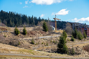 construction crane against the backdrop of an unworthy house on a sunny day among the mountains....