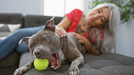 Middle age grey-haired woman with dog smiling confident lying on sofa playing at home