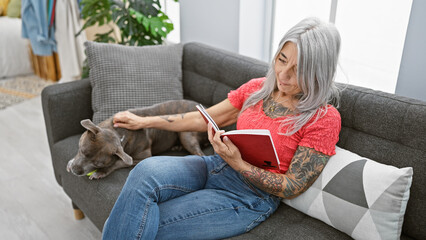 Relaxed middle age woman, a grey-haired bibliophile, snuggled up with her loyal dog, comfortably...