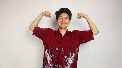 Handsome Asian young man dressed in batik posing with both hands raised, very excited and happy