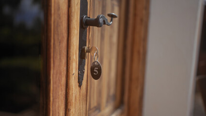 A close-up of an old key in a wooden door's lock, tagged with number 5, evoking a rustic, secure...