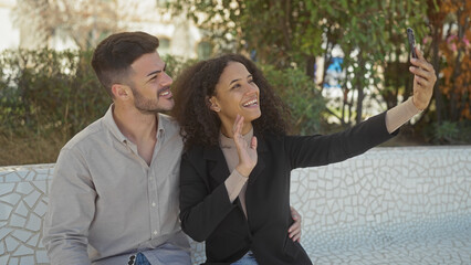 A smiling woman and man take a selfie together in an outdoor park setting, portraying a happy couple moment.