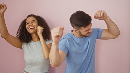 Man and woman joyfully raising fists against a pink wall, expressing success and happiness together.