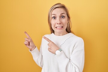 Young caucasian woman wearing white sweater over yellow background pointing aside worried and...