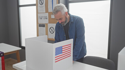 Adult caucasian man with beard voting in a us electoral college room with an american flag