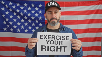 Serious man holding a sign 'exercise your right' in front of an american flag indoors, symbolizing...