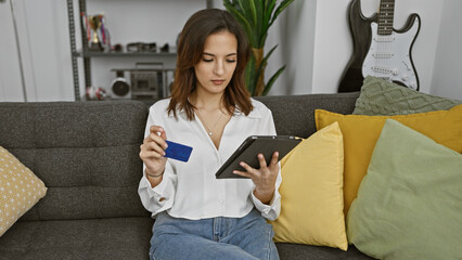 Hispanic woman holding credit card and using tablet in a modern living room