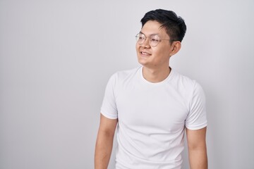Young asian man standing over white background looking away to side with smile on face, natural expression. laughing confident.