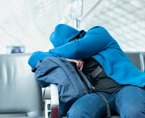 An unrecognizable passenger sleeps hugging his luggage in an airport terminal seat as he waits for boarding time of his flight leaving Paris