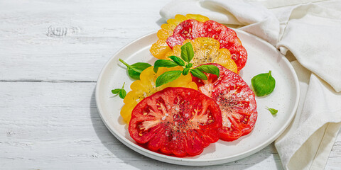 Colorful Heirloom tomato harvest. Ripe ribbed vegetables with fresh basil leaves. Wooden background