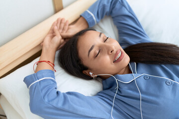 Young arab woman listening to music lying on bed at bedroom