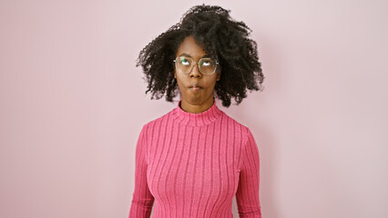 African american woman wearing glasses making a face against a pink background in a studio setting