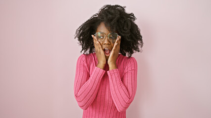 Surprised african american woman wearing glasses and pink sweater indoors against a pink background